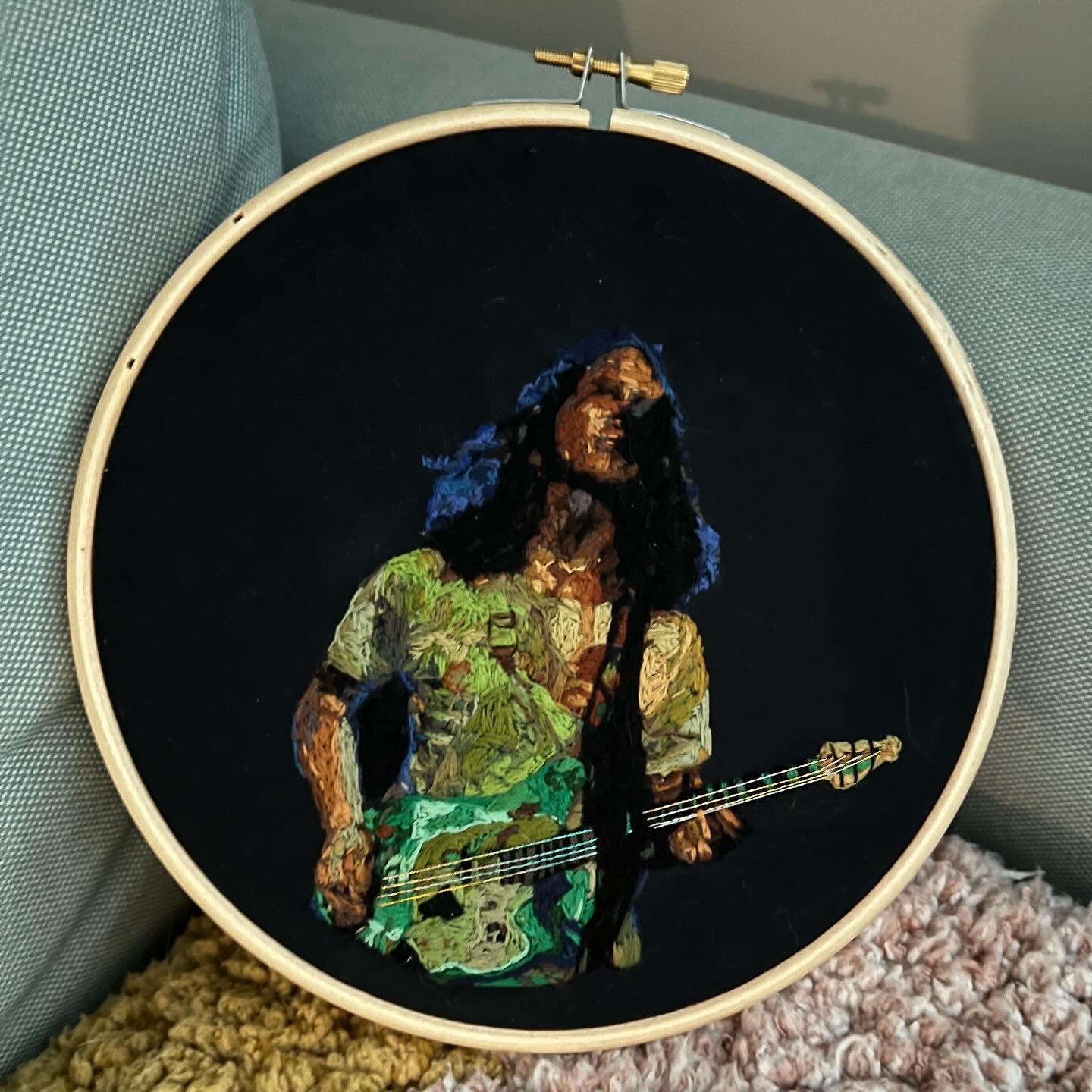 An embroidery hoop depicting a woman playing bass guitar on stage